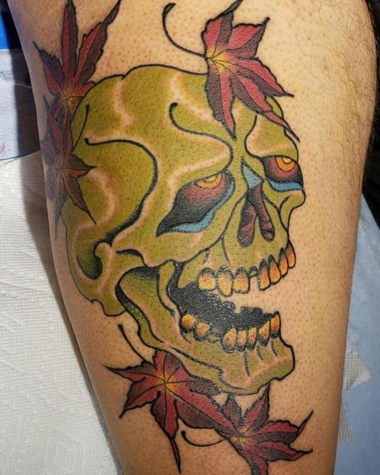 14. Tatuaggio maschile sulla coscia con teschio verde e foglie rosse