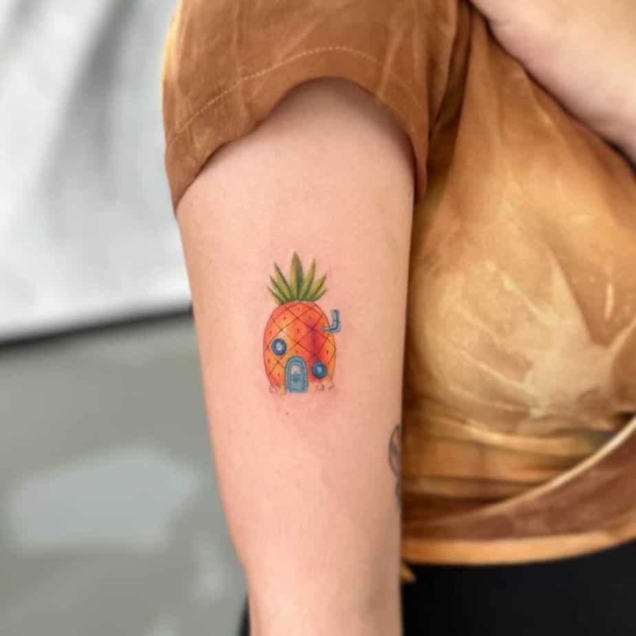 20. Un tatuaggio colorato della casa dell'ananas sulla parte superiore del braccio