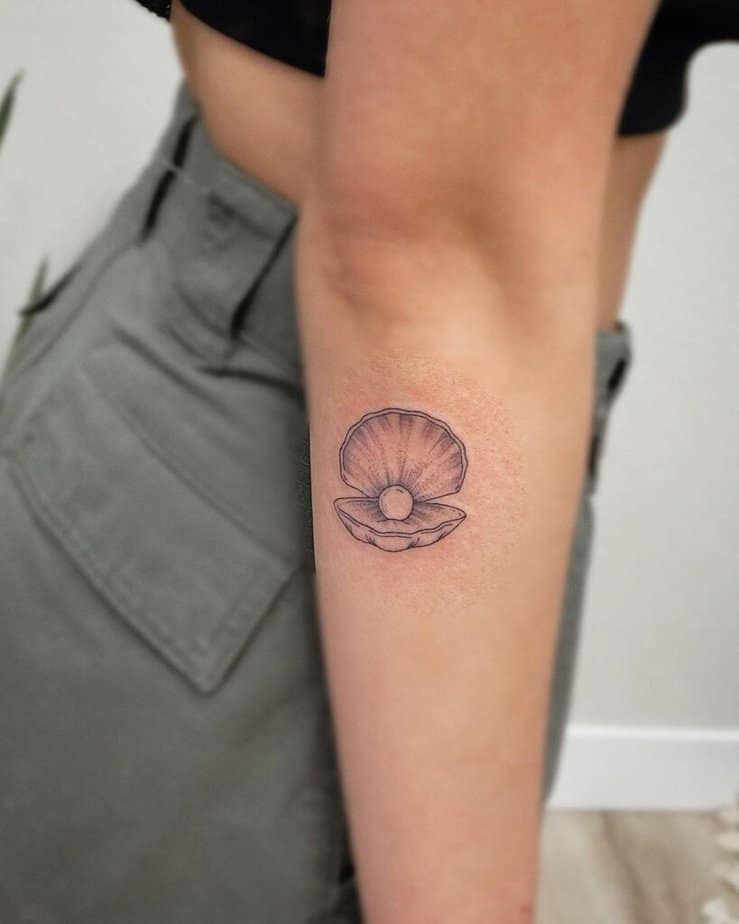 12. A fine-line seashell pearl tattoo on the back of the arm