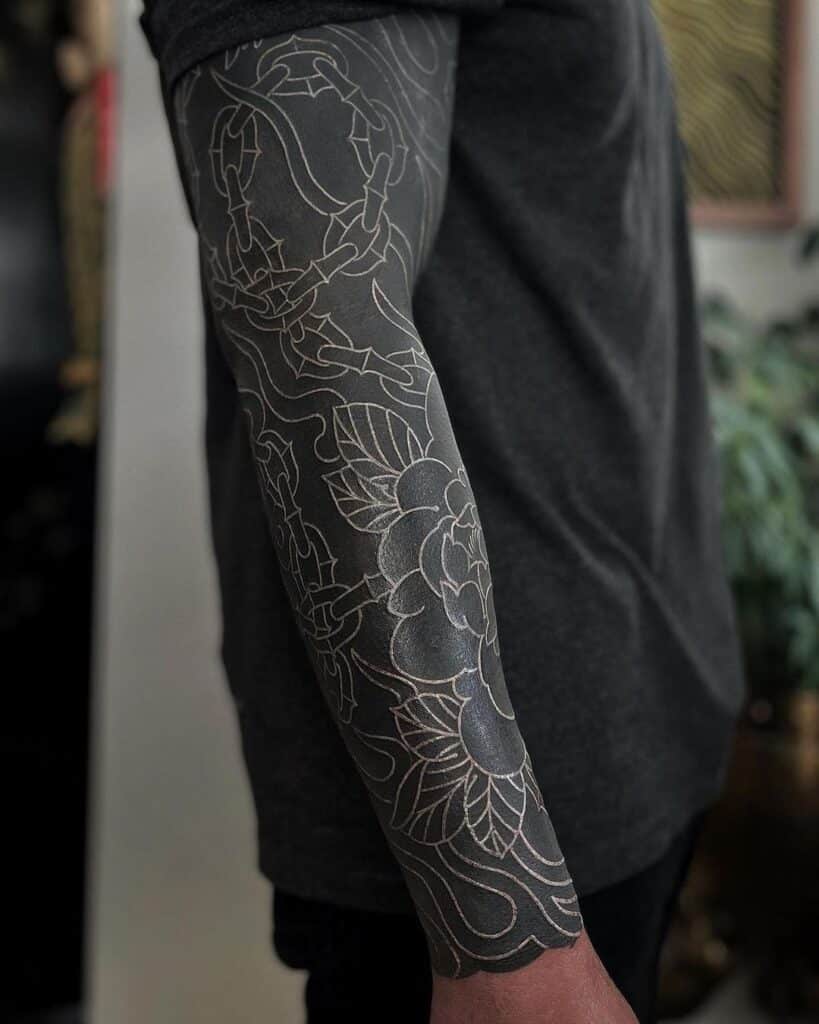 1. Tatuaggio su manica nera con fiori bianchi e catene 