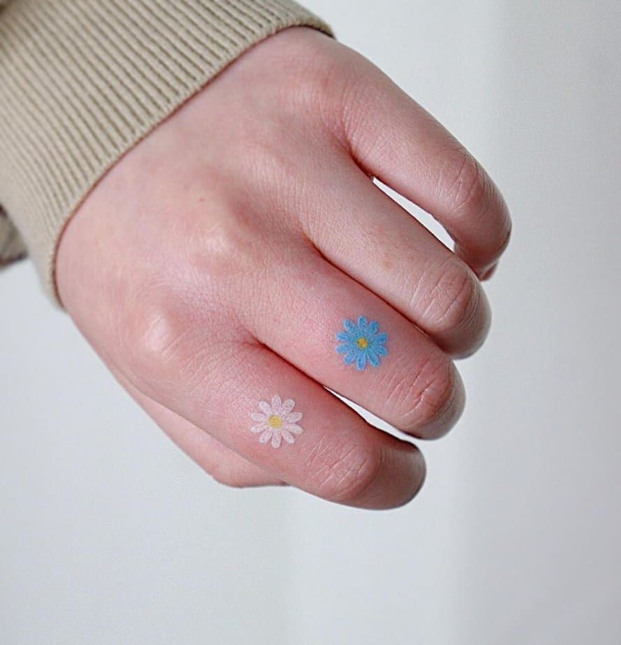 9. Un tatuaggio a forma di margherita blu e bianca sulle dita 