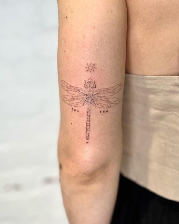 11. Un tatuaggio a forma di libellula, morbido e discreto, sul retro del braccio