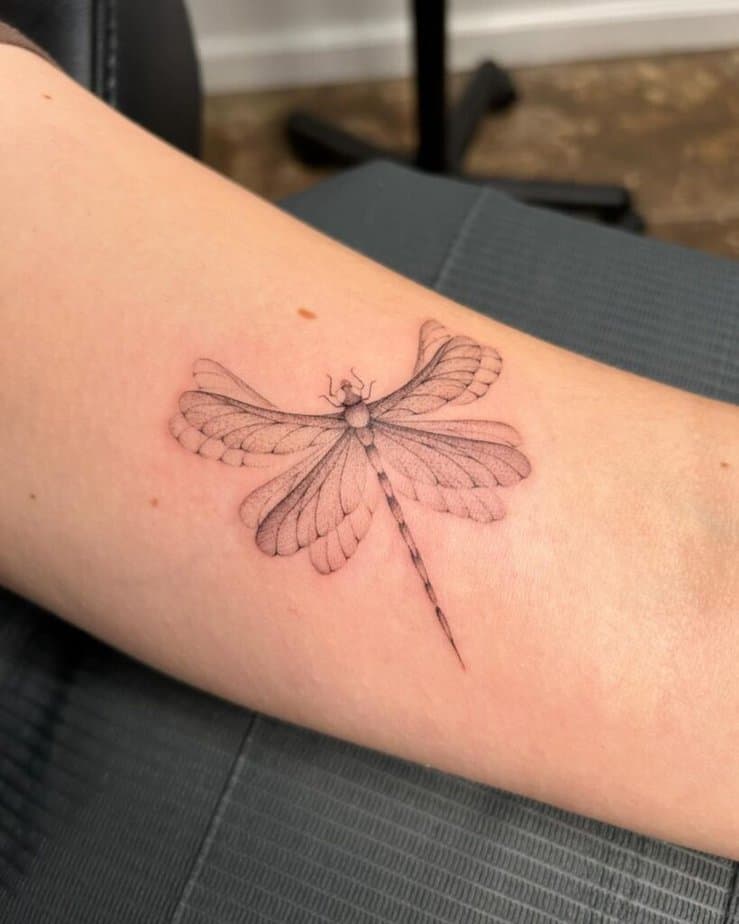 15. Tatuaggio di una libellula svolazzante sul bicipite