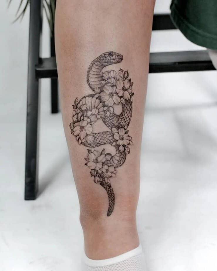 A shin tattoo of a snake surrounded by flowers