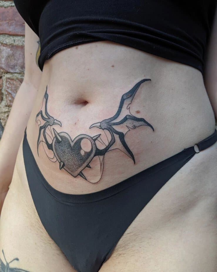 17. A tummy tuck tattoo of a heart with horns and demon wings

