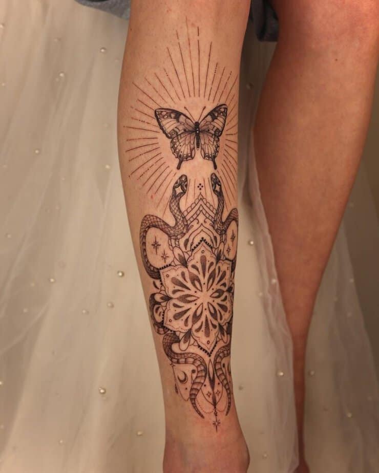 An ornamental shin tattoo with snakes, ornaments, and a butterfly