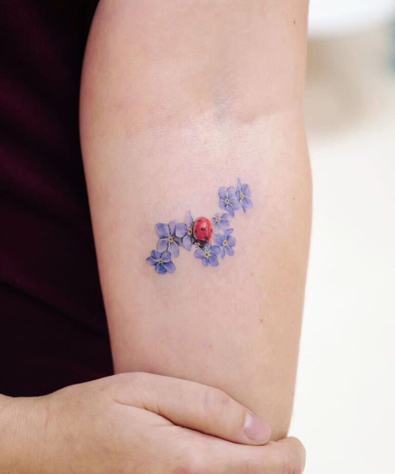 8. Tatuaggio con coccinella e fiore del nontiscordardime
