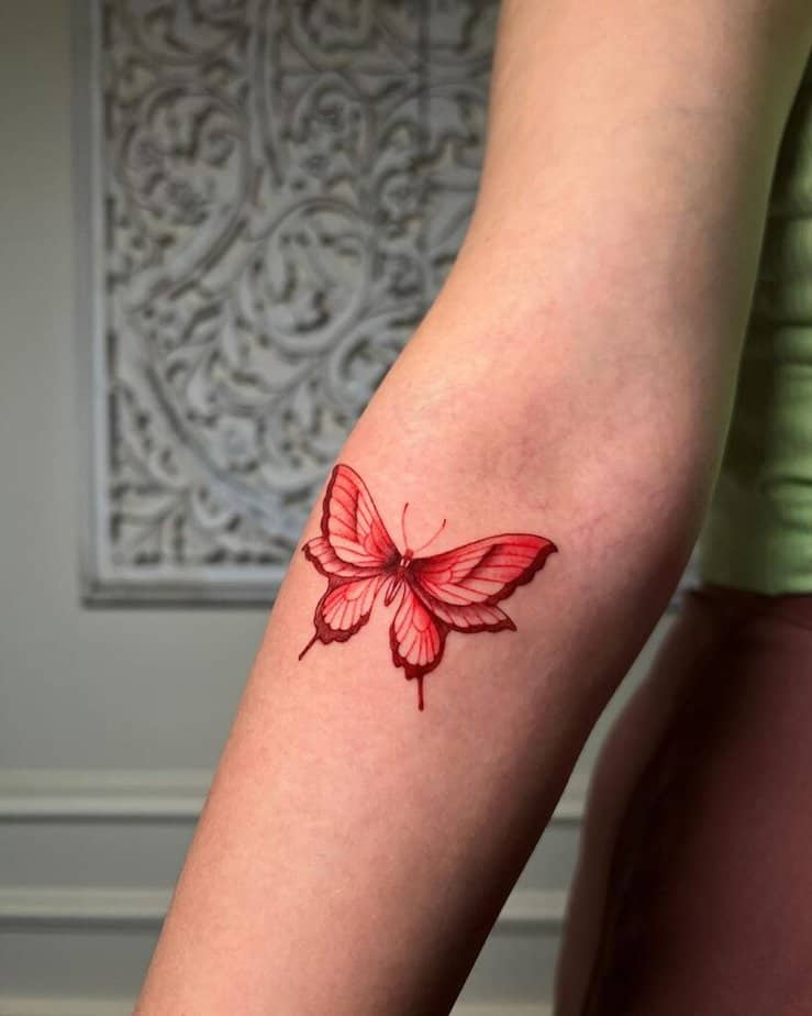 14. A detailed red butterfly tattoo on the forearm