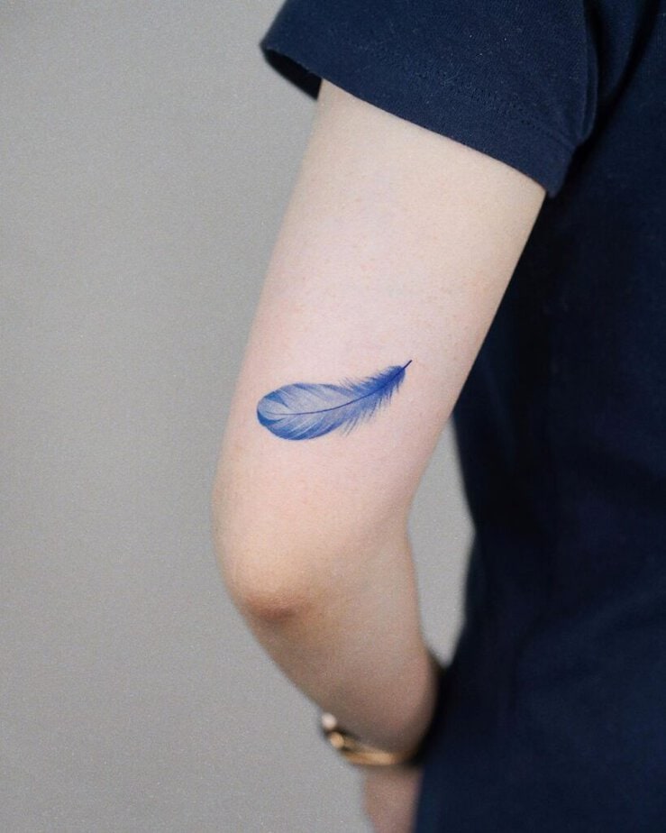 8. Un tatuaggio con una piuma blu sulla parte posteriore del braccio 