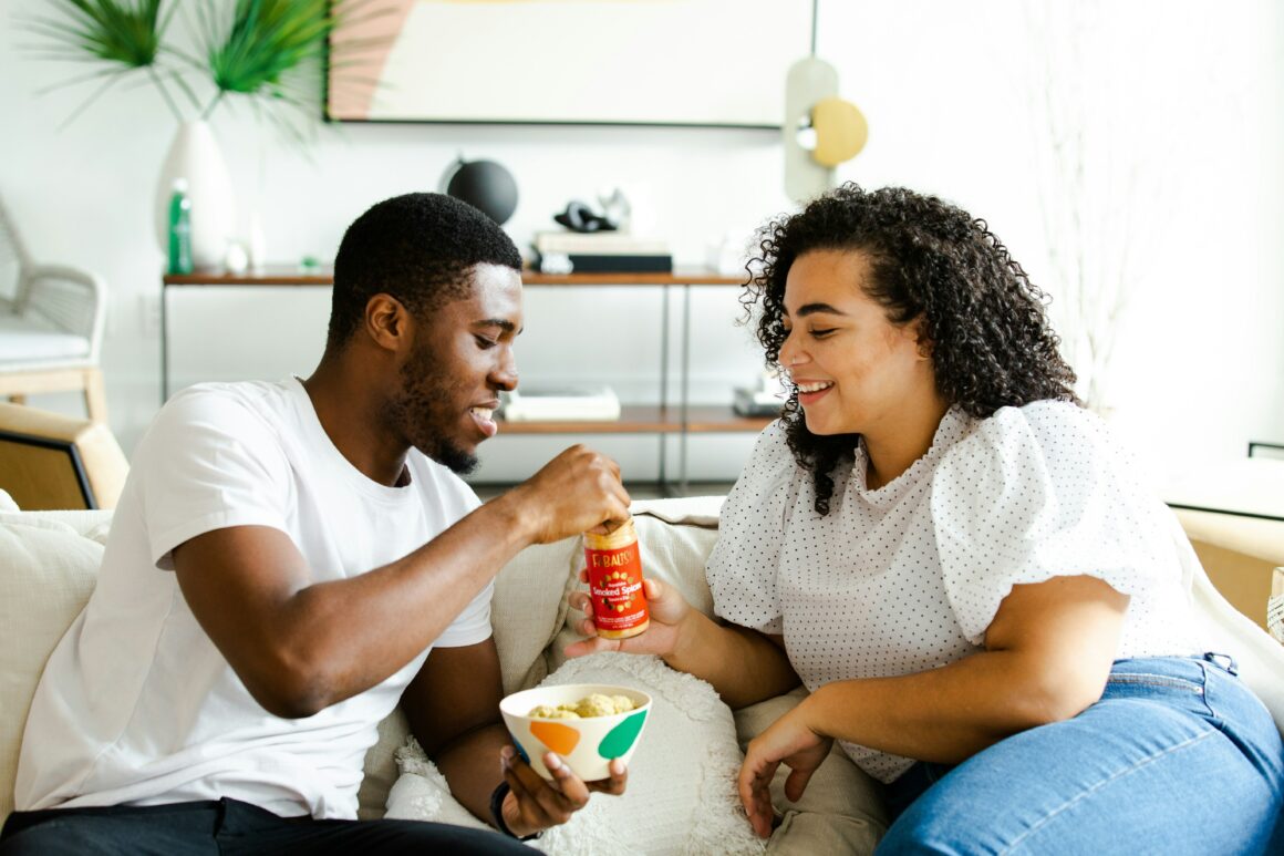 A man and a woman sitting on the couch and eating.