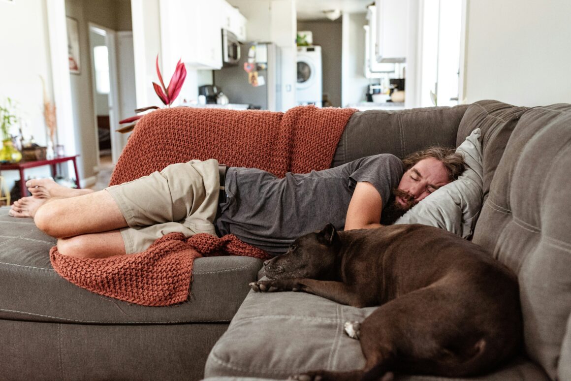 Man sleeping on the couch next to his dog.