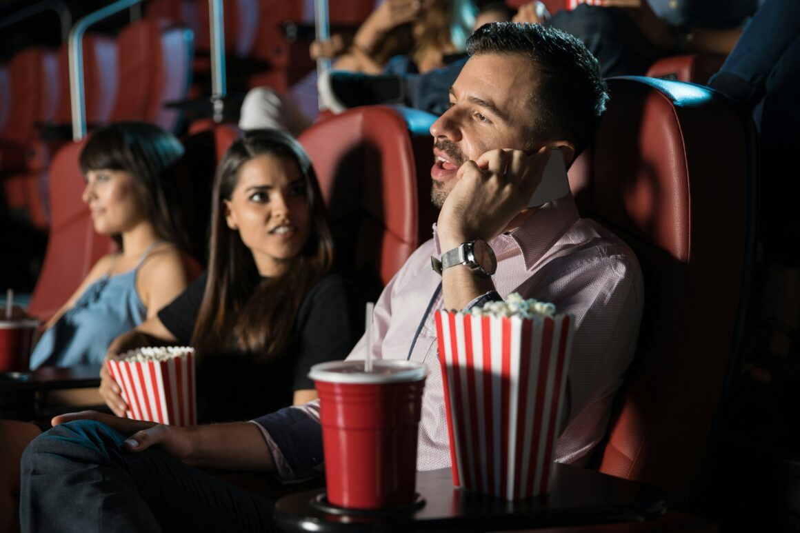 Man talking on the phone while in the movie theater with his partner.